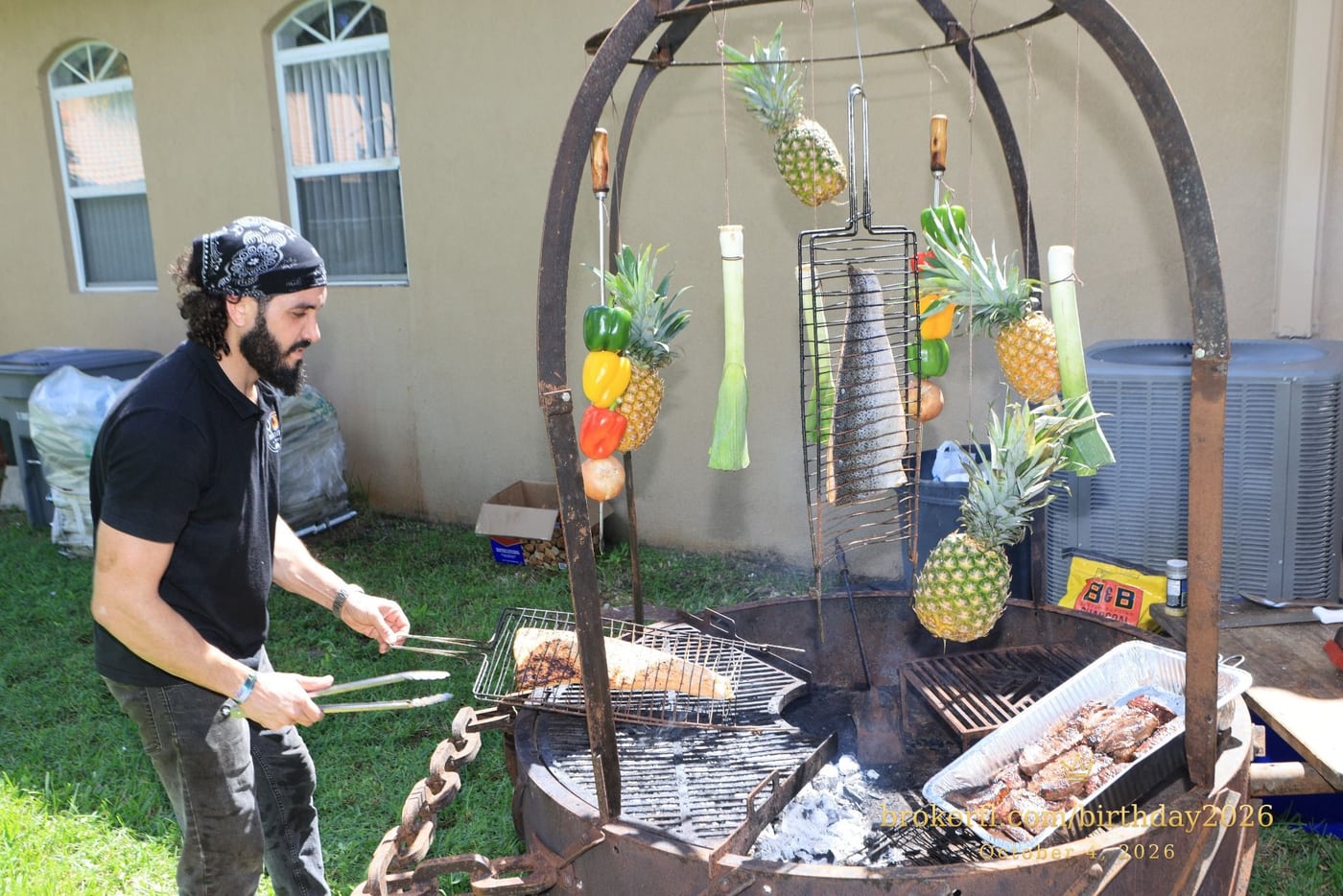 Barbecue cooking over an outdoor fire with hanging vegetables — Karina Leal's birthday, October 4, 2026.
