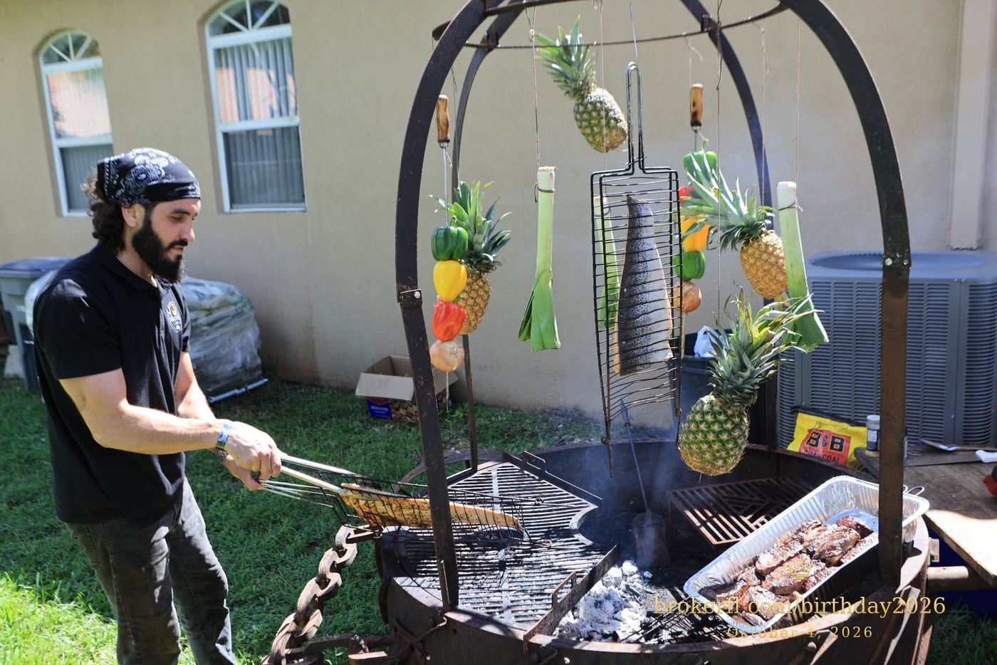 Barbecue cooking over an outdoor fire with hanging vegetables — Karina Leal's birthday, October 4, 2026.