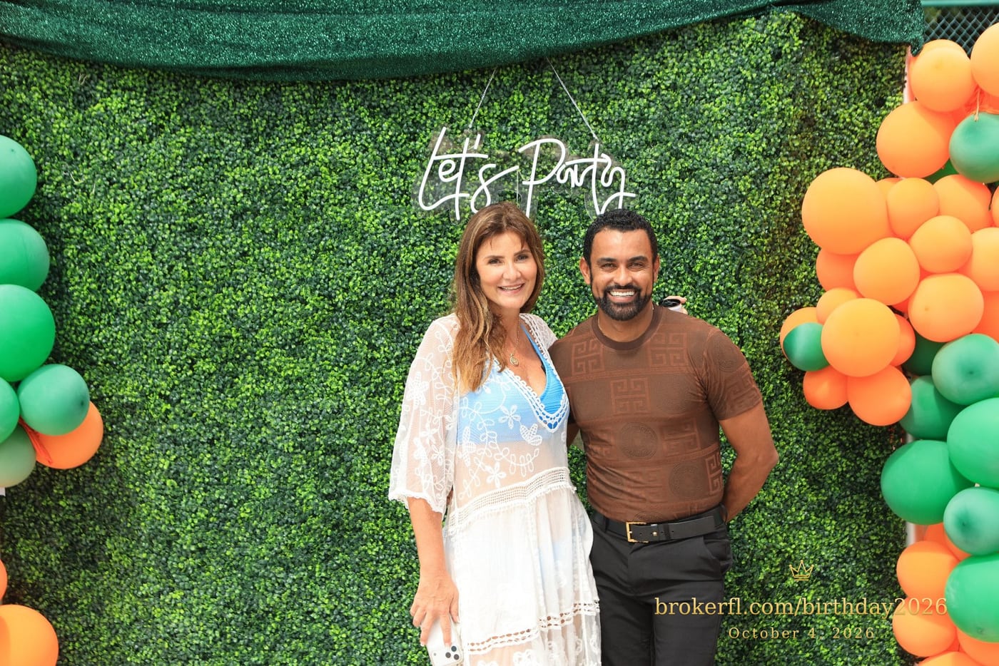 Karina Leal and Edimarcos Silva of Edimarcos Events beside the green and orange balloon backdrop at her birthday celebration in Delray Beach.