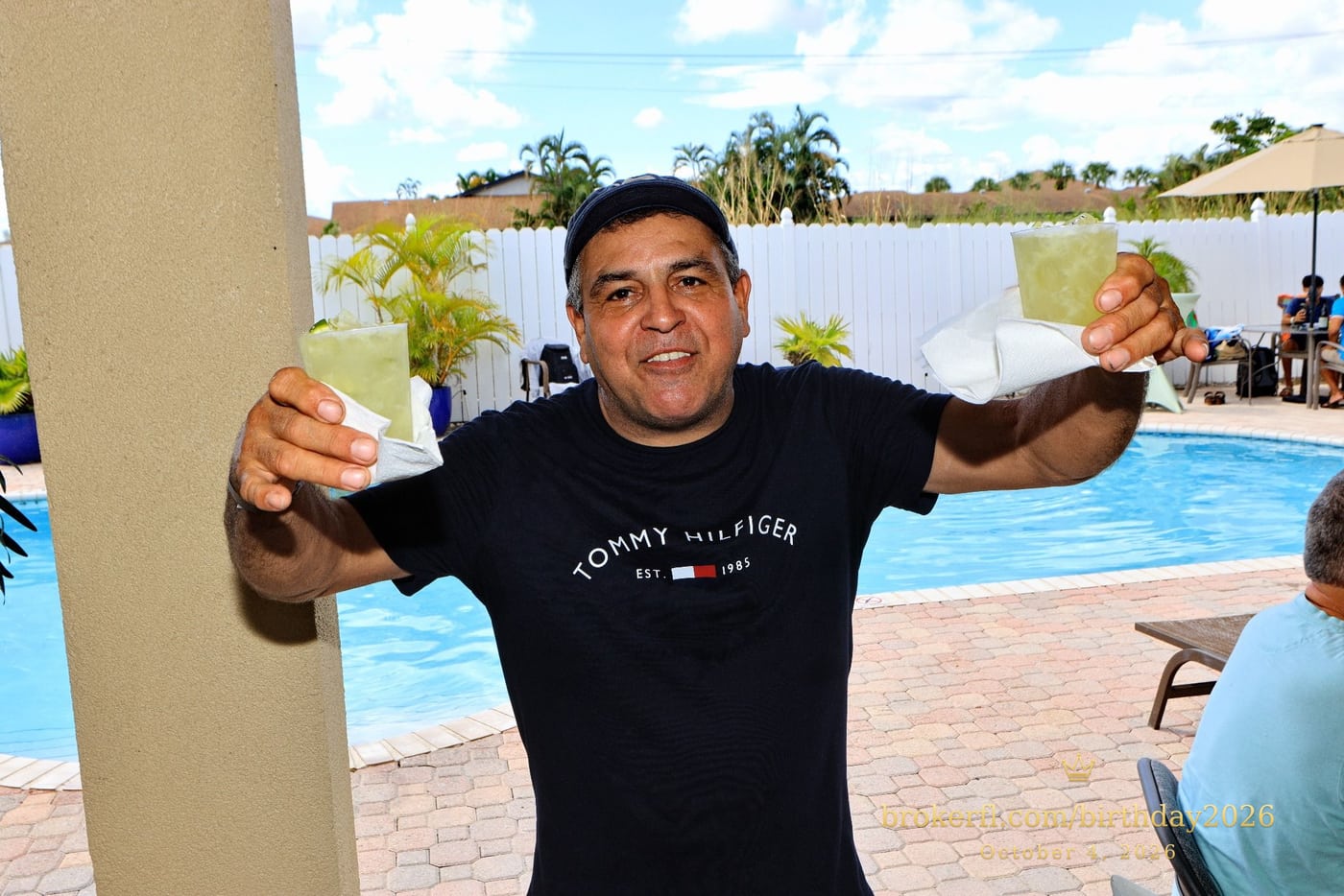 Guest smiling and holding up two drinks beside the pool — Karina Leal's birthday, October 4, 2026.