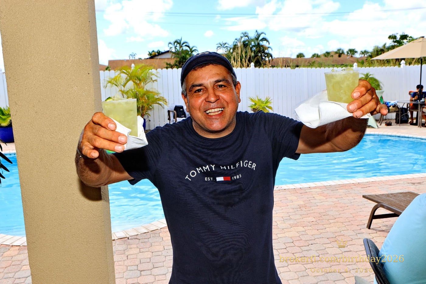 Guest smiling and holding up two drinks beside the pool — Karina Leal's birthday, October 4, 2026.