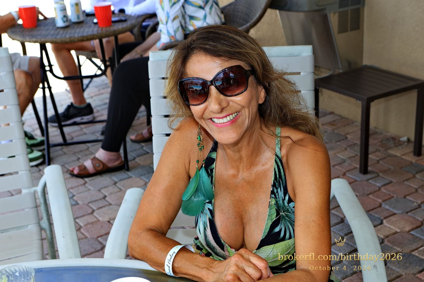 Guest in a tropical print outfit smiling at a patio table — Karina Leal's birthday, October 4, 2026.