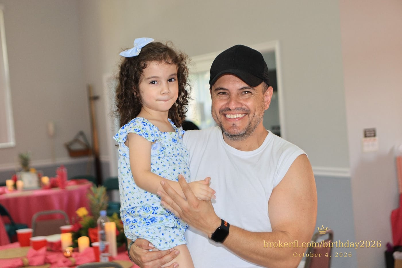 Adult holding a smiling young guest in a blue dress — Karina Leal's birthday, October 4, 2026.