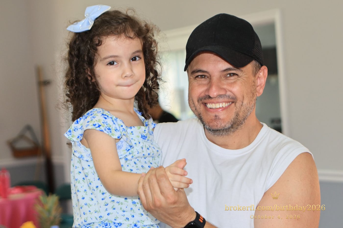 Adult holding a smiling young guest in a blue dress — Karina Leal's birthday, October 4, 2026.
