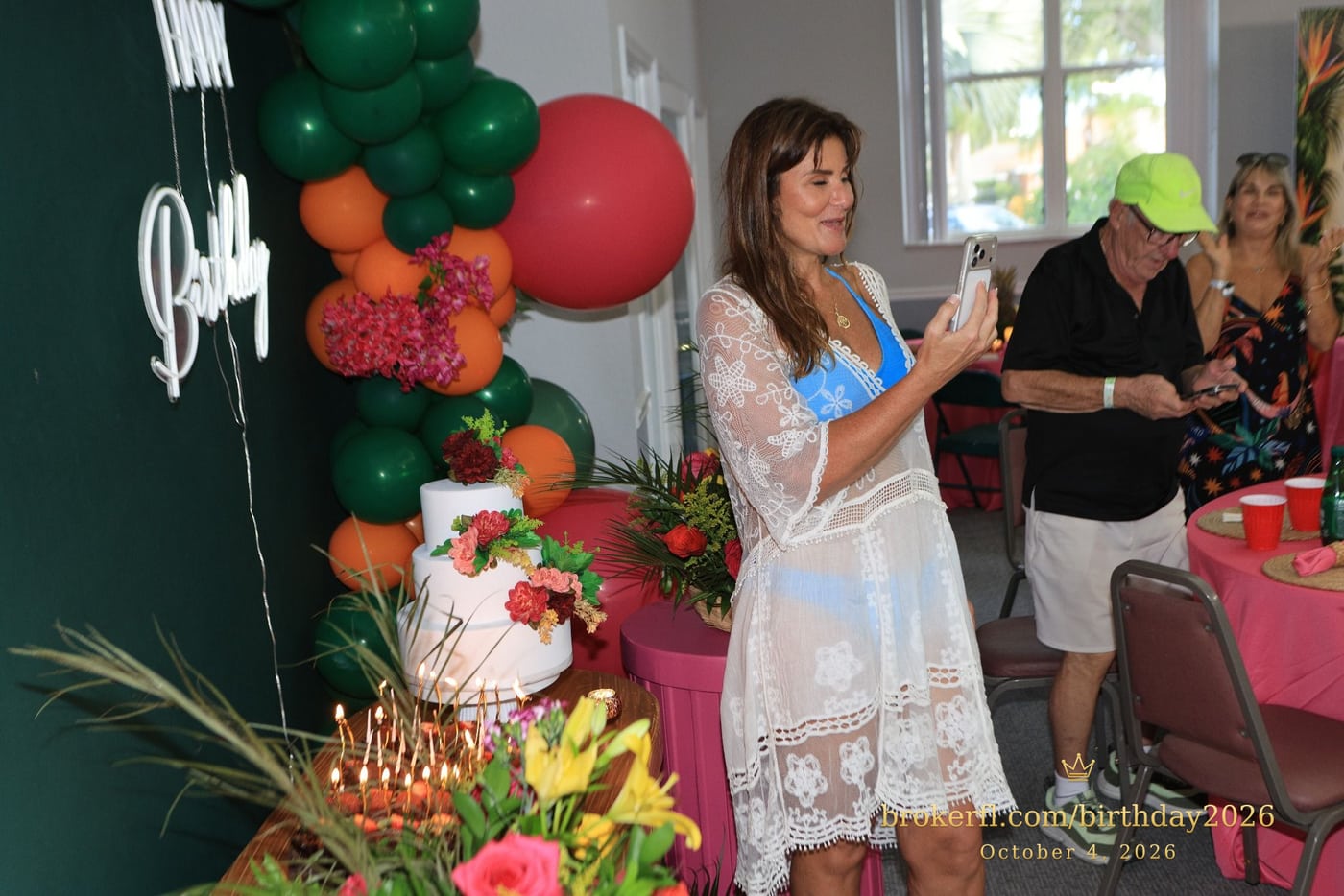 Guest in a white lace cover-up celebrating beside the birthday cakes — Karina Leal's birthday, October 4, 2026.