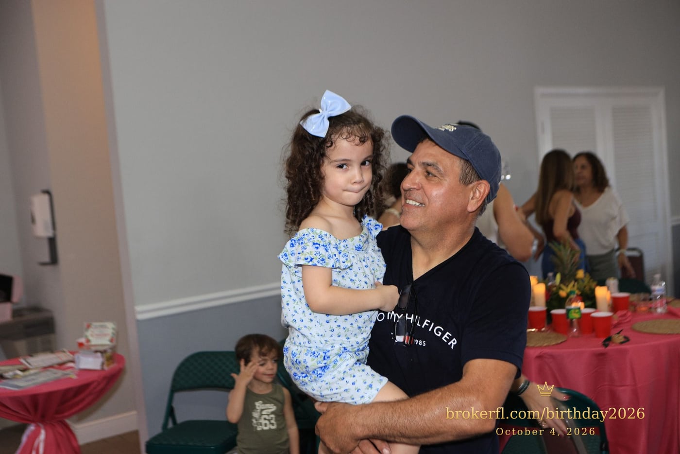 Adult holding a young guest in a blue dress at the celebration — Karina Leal's birthday, October 4, 2026.